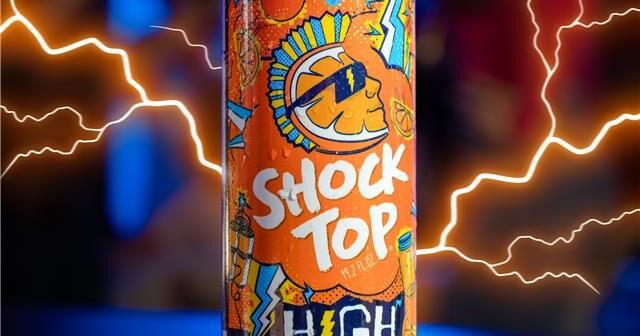 Shock Top High Voltage beer can, featuring an orange background with a blue and yellow mohawk-wearing orange slice mascot against stylized lightning bolt backdrop.