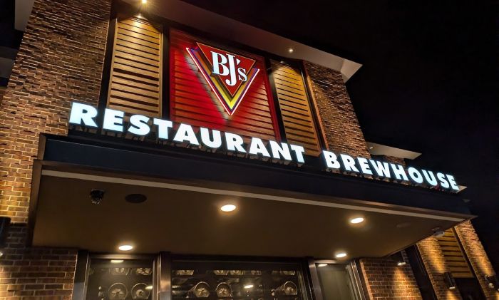 An exterior shot of BJ's Restaurant & Brewhouse at night, showcasing the illuminated red logo and large neon lettering above the entryway.