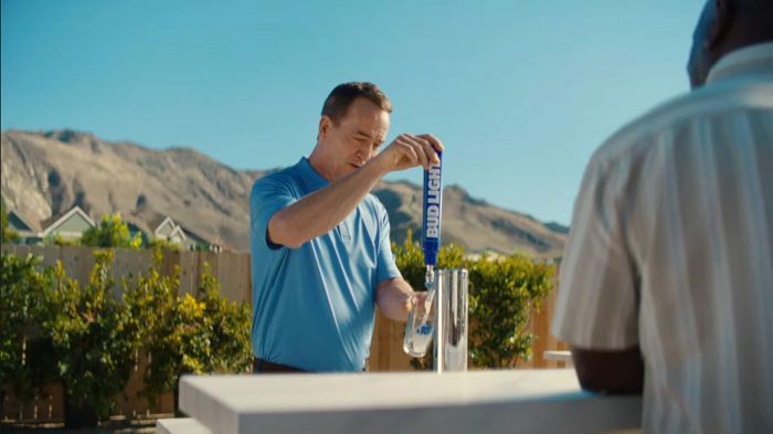 Peyton Manning pours a Bud Light from a tap at an outdoor bar with mountains in the background.