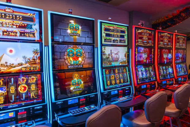 Rows of brightly lit slot machines with colorful immersive themes and interactive displays in a modern online gaming-inspired casino environment.