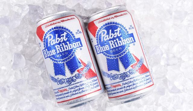 You said: Concise alt text for image:Two cans of Pabst Blue Ribbon beer rest on a bed of crushed ice.