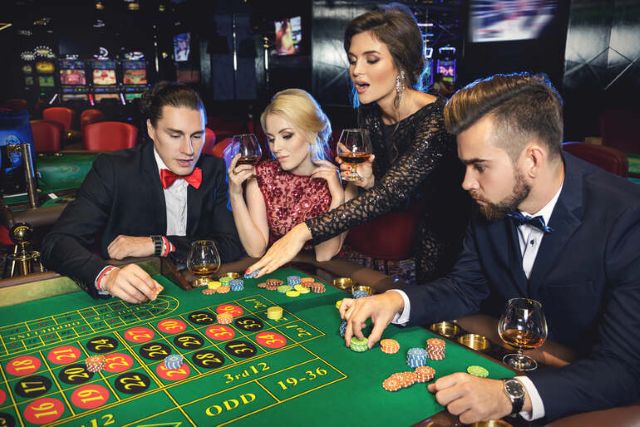 Friends playing beer-themed casino games at a roulette table while enjoying drinks in a lively casino.