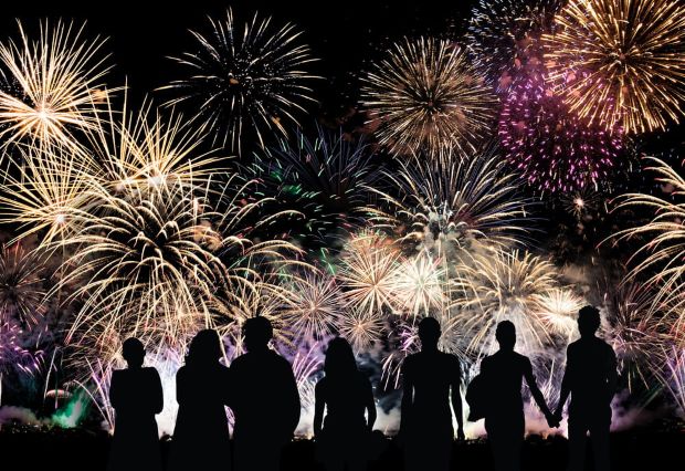Silhouettes of a crowd of people watching a large, colorful fireworks display filling the night sky.