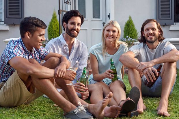 Friends enjoying bottled beer while relaxing on a front lawn, illustrating the social side of planning a beer-focused trip the Canadian way.