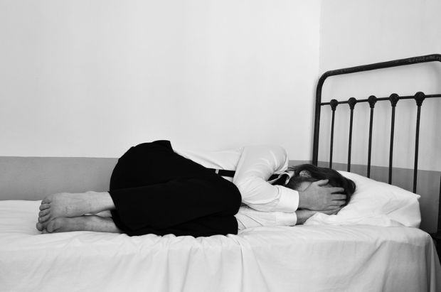 Person lying curled up on a bed, illustrating abuse and neglect in psychiatric facilities.