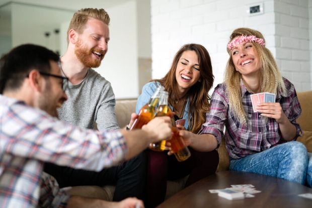 Friends enjoying a craft beer game night with drinks and playing cards at home.