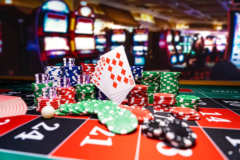 Casino table with playing cards and stacks of chips, with slot machines in the background illustrating better odds at table games.