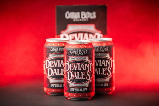 Three cans and a cardboard package of Oskar Blues Brewery's "Deviant Dale's Imperial IPA" set against a vibrant red background.