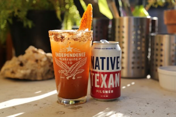 An Independence Brewing michelada in a chili-rimmed glass next to a can of Native Texan Pilsner.