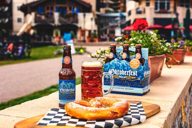 Breckenridge Oktoberfest beer bottle, six-pack and stein of amber lager with a soft pretzel at an outdoor beer garden.
