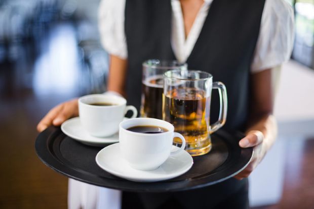 A waitress holding a serving tray of beer and coffee.