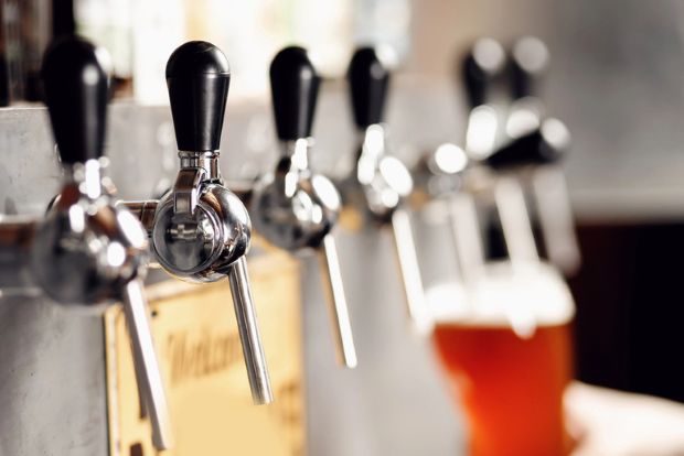 A bar with stainless steel beer holders in a row pouring fresh craft beer into beer mugs.