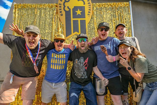 Celebrating medal winners at the 2026 Great American Beer Festival in Denver, five brewery team members cheer and pose with bronze medals in front of a gold GABF backdrop.