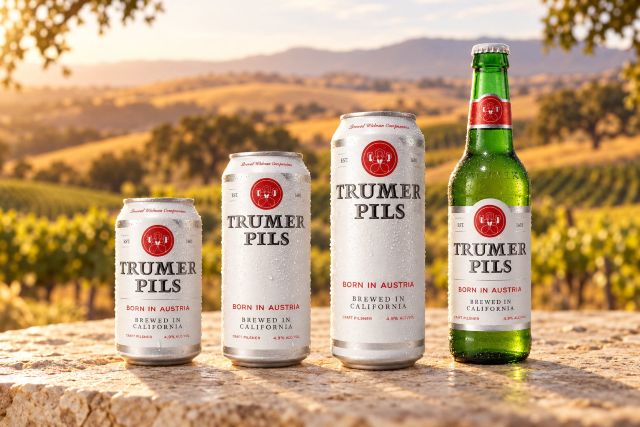 Three Trumer Pils cans and a green bottle on a stone tabletop, with vineyards and golden California Central Coast hills in the background.
